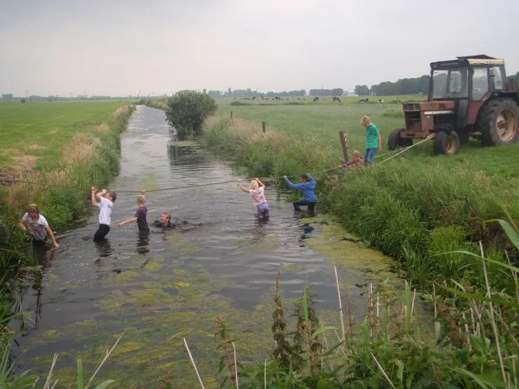 Kinderen spelen in de sloot naast de tractor
