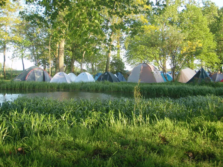 Rij tenten naast de watergang omgeven door weelderig groen